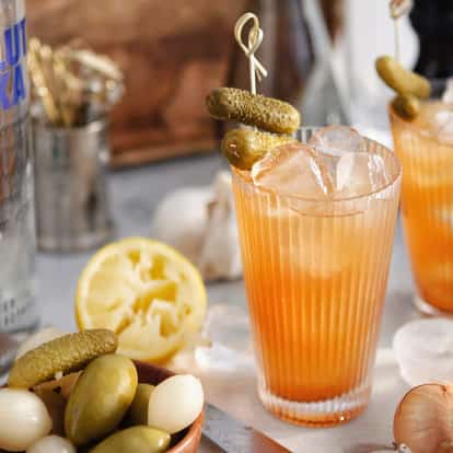 Pickle Brine Bloody in a highball glass with a cornichon skewer and an Absolut Vodka bottle in background