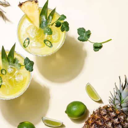 Pineapple Cooler two glasses with ice, pineapple wedges, jalapeño slices and cilantro on white background