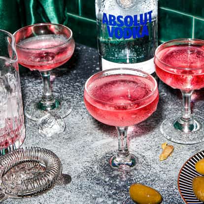 Three stunning Pink Martini cocktails next to a bottle of Absolut Vodka.