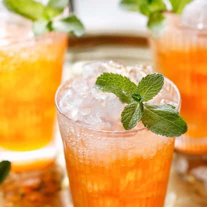 Planter’s Punch in three highball glasses with crushed ice and mint sprigs on a metal tray