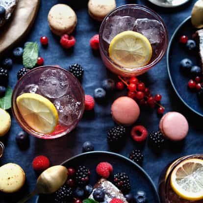 Poinsettia served in stemless glasses with lemon slice and ice surrounded by berries macarons and plates on cloth