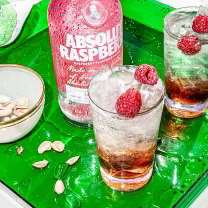 Raspberry Collins in two collins glasses with ice, raspberries and an Absolut Raspberry bottle