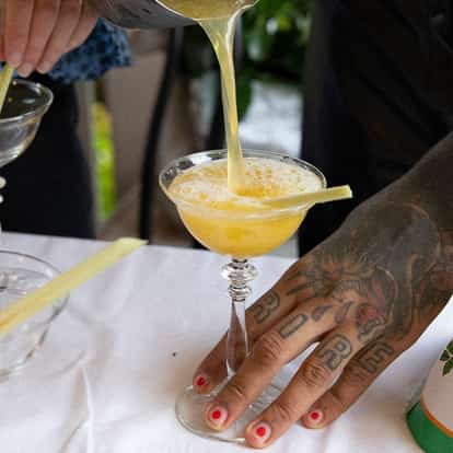 Rogue Lemongrass in a stemmed coupe with liquid pouring and a lemongrass stick on the rim, Absolut vodka bottle at left