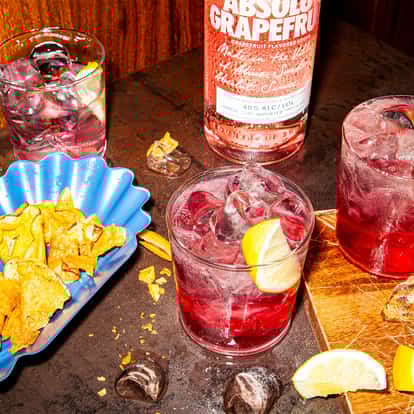Rose Kennedy Cocktail in a rocks glass with lemon wedge and ice, next to an Absolut Grapefruit bottle on a wooden table
