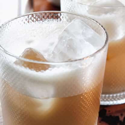 Russian Recycled served in two textured rocks glasses with ice and a layer of foam on a wooden tray