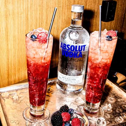 Russian Spring Punch in two glasses with crushed ice and berry garnish on a tray beside an Absolut bottle