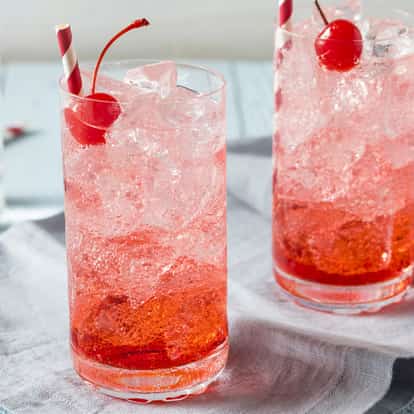 Two Shirley Temple drinks filled with ice and garnished with a red cherry.