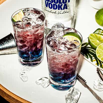 Sparkler in two highball glasses with crushed ice and lime wedges and an Absolut vodka bottle in background