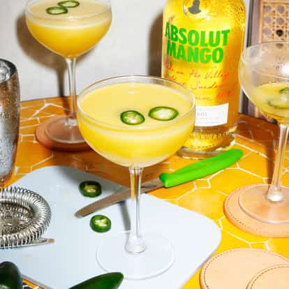 Spicy Mangotini in a coupe glass with jalapeño slices next to an Absolut Mango bottle on tiled table