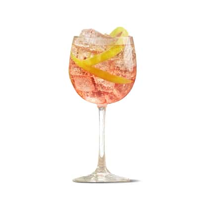 Strawberry Punch in a wine glass with ice and a lemon peel on white background