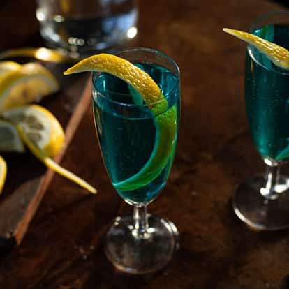 Strong Arm in two champagne flutes with lemon twists on a wooden table