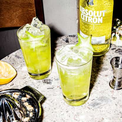 Summer Love in two highball glasses with ice and starfruit garnish and an Absolut Citron bottle on marble