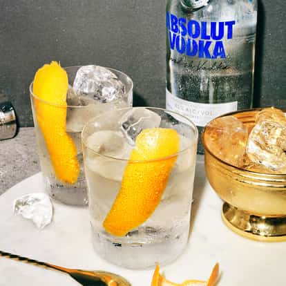 Summertime Cookout in two rocks glasses with ice and orange peels and Absolut Vodka bottle in background on marble
