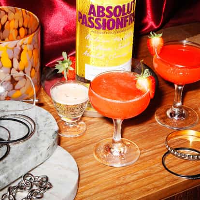 Sunset Martini in two coupe glasses garnished with strawberry halves with an Absolut Passionfruit bottle behind