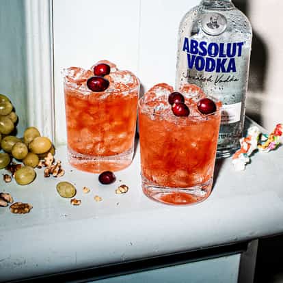 Sweetheart two rocks glasses filled with crushed ice and cranberries beside an Absolut Vodka bottle