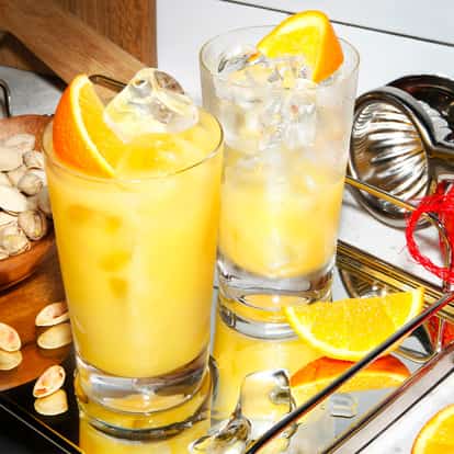 Tequila Screwdriver served in two ice-filled highball glasses with orange wedges on a mirrored tray