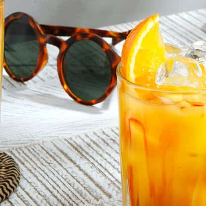 Tequila Sunrise cocktail garnished with an orange wedge next to a pair of sunglasses.
