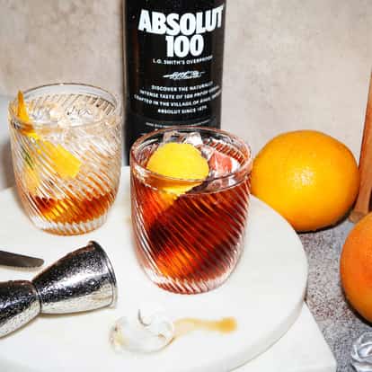 The 100 Negroni served in two ribbed rocks glasses with ice and orange peel and an Absolut 100 bottle behind