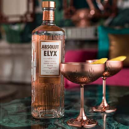 The Elyx Martini served in two coupe glasses with lemon twists and an Absolut Elyx bottle on a table