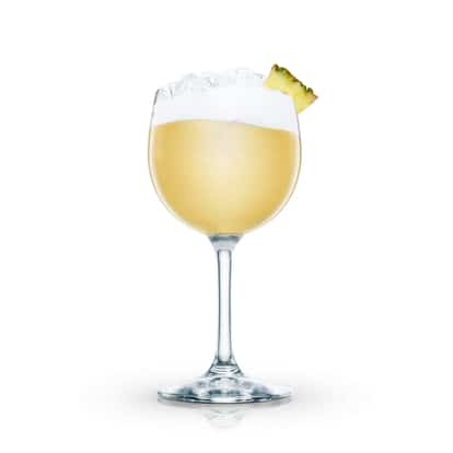 Tropical Colada in a wine glass with crushed ice, foam and a pineapple wedge
