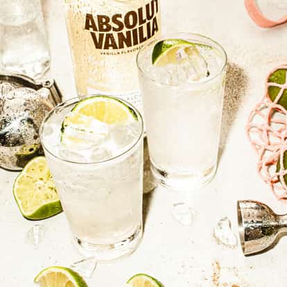 Vanilla Rain served in two highball glasses with ice and lime wedges, Absolut Vanilla bottle in background