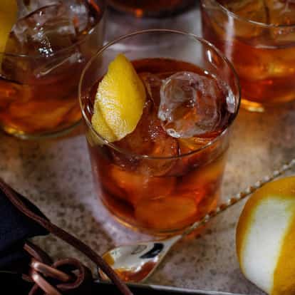 Vieux Carré served in a rocks glass with large ice cubes and a lemon peel garnish on a metal tray