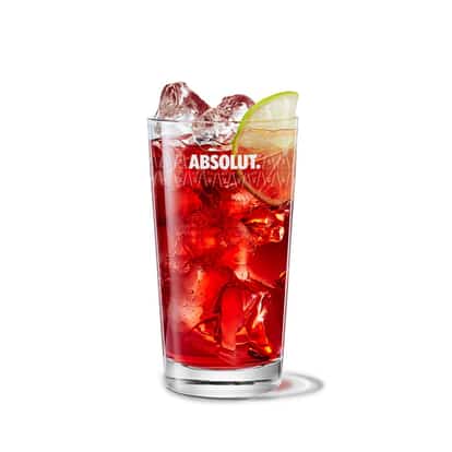 Vintage Cape Codder in an Absolut highball glass with ice and a lime wedge on white background.