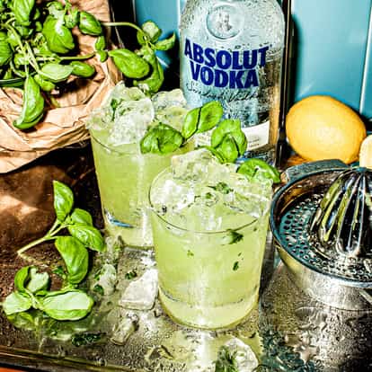 Two Vodka Basil Smash cocktails next to a bottle of Absolut Vodka.