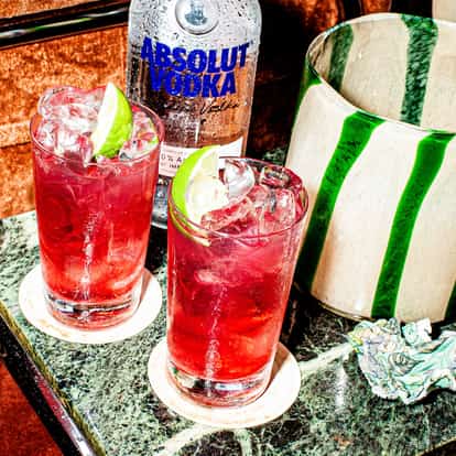 Two Vodka Cranberry cocktails next to a bottle of Absolut Vodka.