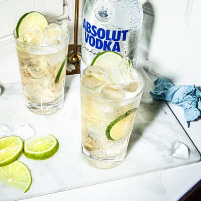 Vodka Ginger Ale next to a bottle of Absolut Vodka and fresh limes