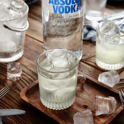 Vodka Iceberg in a ribbed rocks glass with ice beside an Absolut Vodka bottle on a wooden table