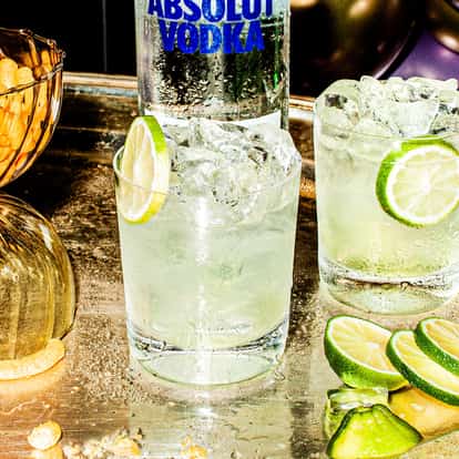 Vodka Lime in two rocks glasses with ice and lime slices on a metal tray with an Absolut Vodka bottle visible