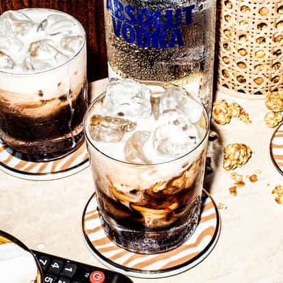 Two White Russian cocktails in rocks glasses next to a bottle of Absolut Vodka