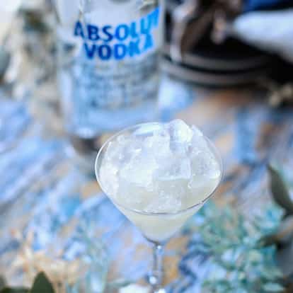 X-rated cocktail in a stemmed coupe topped with crushed ice and an Absolut vodka bottle in the background.