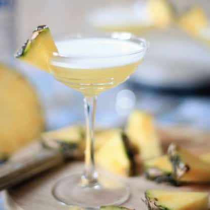 Yang Tze in a coupe glass garnished with a pineapple wedge on a wooden board