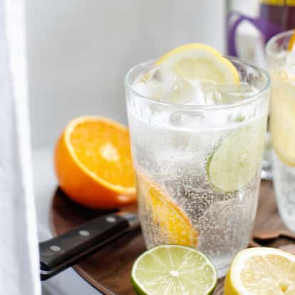Three citrus drinks in tall glasses garnished with lemon, lime and orange slices.