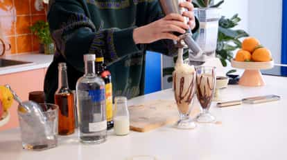Frozen Espresso Martini cocktails in a milkshake glass being garnished with whipped cream next to a bottle of Absolut Vodka