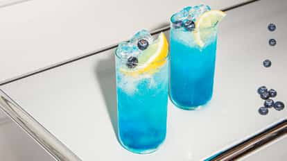 Blueberry Fizz cocktails served in tall, chilled glasses, vibrant blue and packed with ice, garnished with lemon wedges and fresh blueberries.