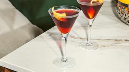 Two martini glasses filled with a dark red cocktail and lemon twists on a bright marble countertop.