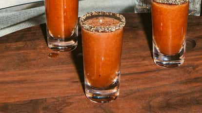 Shot Bloody Mary en vaso transparente con borde de pimienta sobre mesa de madera, color rojo intenso.