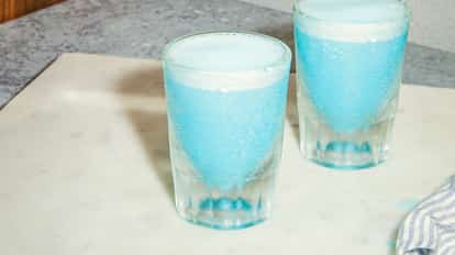 Two frosty glasses of the Blue Jay cocktail, light blue and foamy, served chilled on a stone surface.