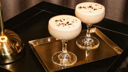 Blushin Russian en copas coupe con virutas de chocolate sobre una bandeja dorada junto a una lámpara.