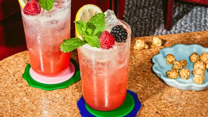 Zwei Campari-Nobile-Cocktails mit Eis, Himbeeren, Brombeeren, Zitronenscheiben und frischer Minze in hohen Gläsern auf bunten Untersetzern.