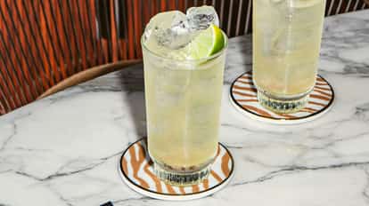 Firework drink in tall ice-filled glasses with lime wedges on patterned coasters on a white marble table.