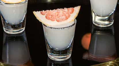 Grapefruit Drop shot served in a clear shot glass with a grapefruit wedge on top, placed on a glossy black surface.