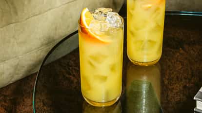 Harvey Wallbanger cocktail in a tall glass with ice and orange slice garnish, golden drink on a dark glass table in a stylish bar setting.