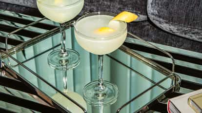 Lemon Martinis in coupe glasses with fresh lemon peel on a mirrored tray over a metal surface.