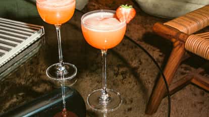 Mayday Martini cocktail in coupe glasses with frothy pink foam and strawberry garnish, set on a glass table in a stylish lounge.