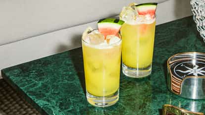 Melon Ball cocktails in highball glasses with fresh watermelon slices on a green marble surface.