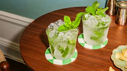 Dos cócteles mint julep con hielo picado y menta, servidos en vasos texturizados sobre posavasos de cuadros verdes.